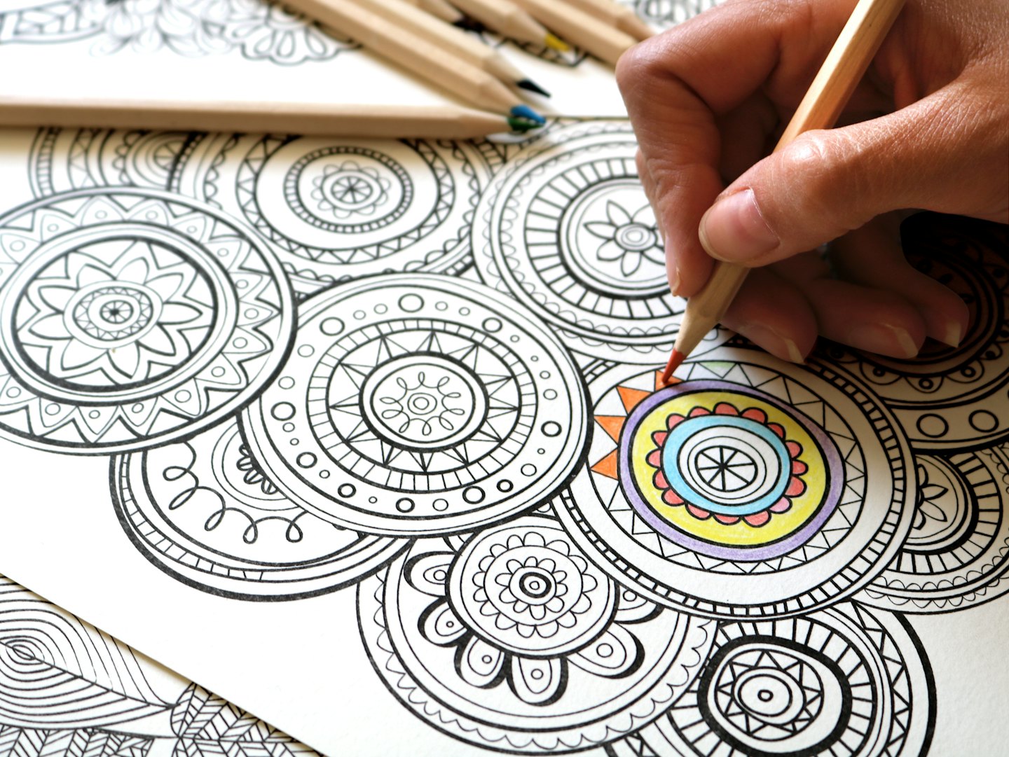 Eine Person malt ein Mandala-Muster mit einem roten Stift aus.