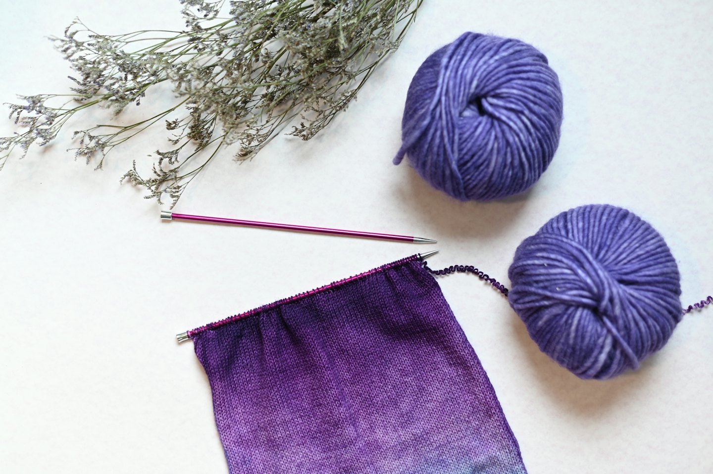 Strickarbeit mit mehrfarbigem lila Garn und rosa Nadeln.