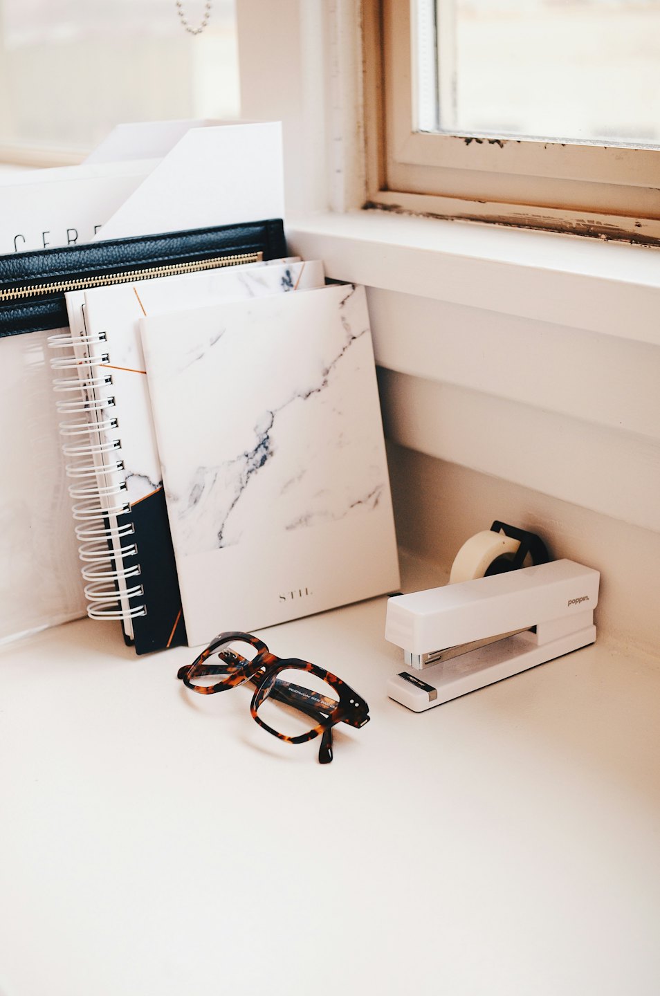 Notizbücher, Brille, ein Tacker und ein Klebebandabroller auf einem Schreibtisch.