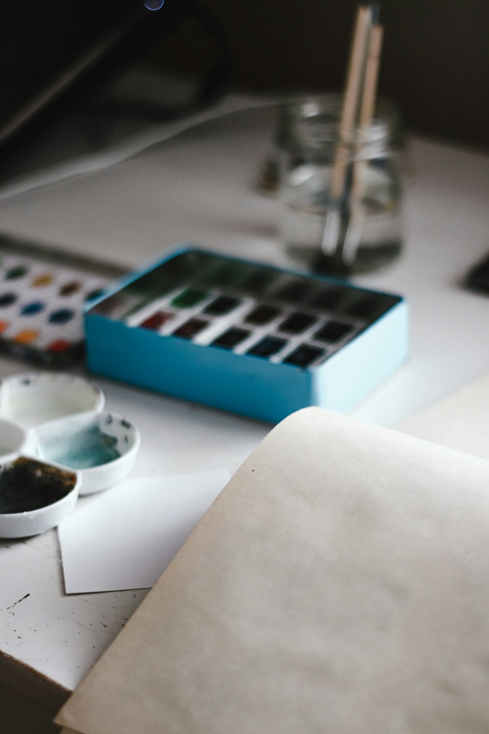 Aquarellfarben-Zubehör auf einem weißen Schreibtisch mit Pinseln und Papier.