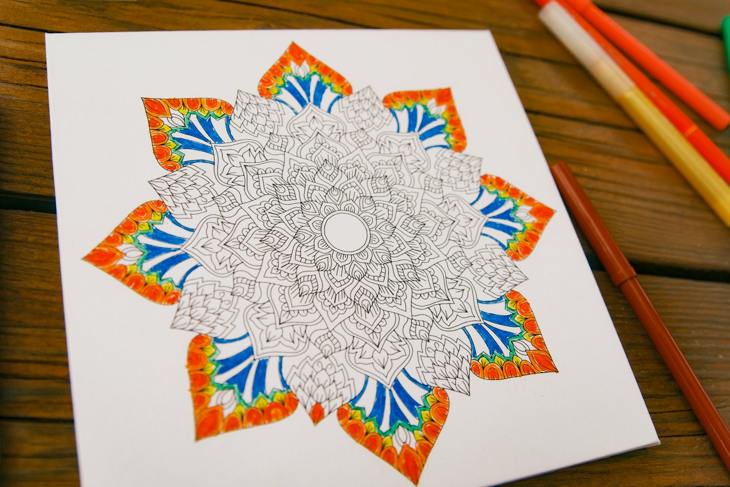 Ein teilweise gefärbtes Mandala-Design steht auf einem Holztisch.