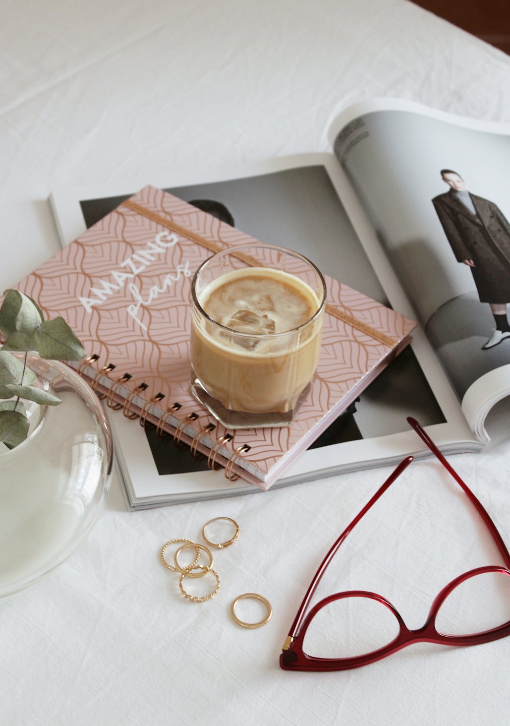 Eiskaffee, Notizbuch und Brille auf einer Zeitschrift.