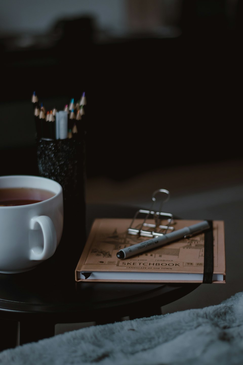 Teetasse, Buntstifte und Skizzenbuch auf einem Tisch.